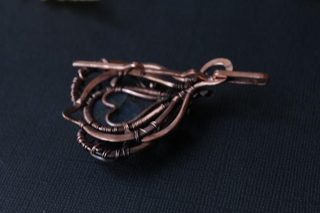 A handcrafted wire sculpture shaped into a heart, intricately twisted and placed on a dark background.