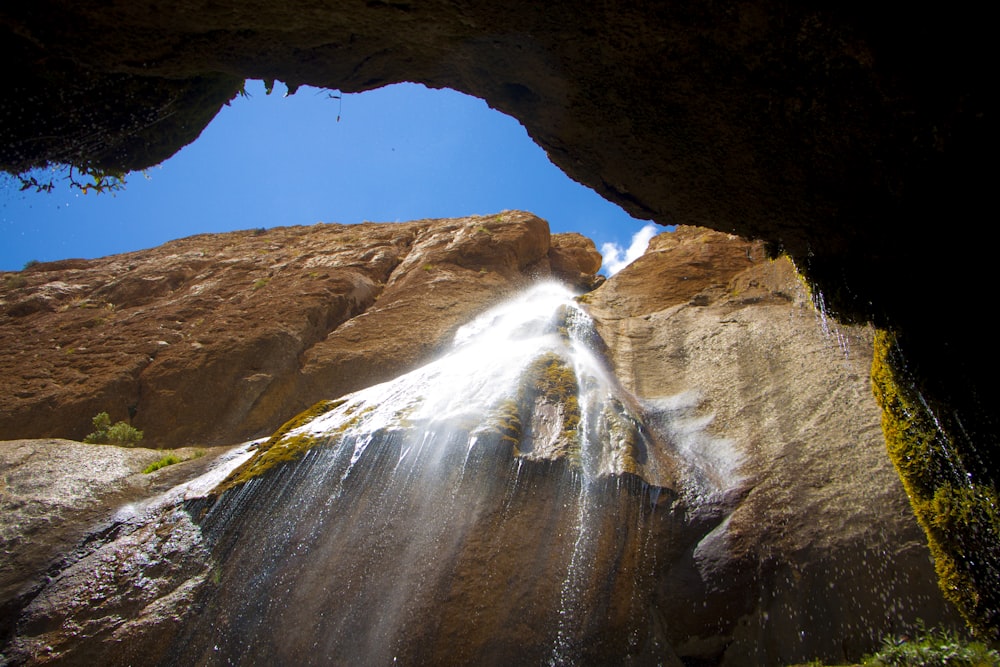 a waterfall coming out of a cave into a blue sky