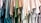 A collection of colorful t-shirts hanging closely together, arranged in a row. The shirts display a variety of shades, including blues, greens, and neutral tones. The material appears casual and lightweight, suitable for everyday wear.