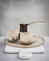 A close-up of handcrafted ceramic mugs with subtle textures, resting on a simple wooden tray.