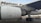 Close-up view of an airplane's engine and landing gear on the tarmac. The logo of an airline is visible on the body of the aircraft. In the background, there are service vehicles.