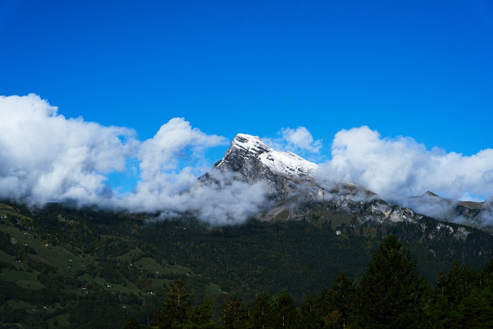 a mountain covered in clouds with a snow capped peak in the distance