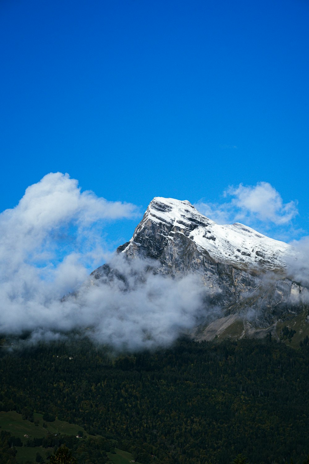 a mountain covered in snow and clouds under a blue sky