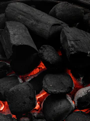 Close-up of glowing coconut shell charcoal pieces arranged on a rustic wooden surface.