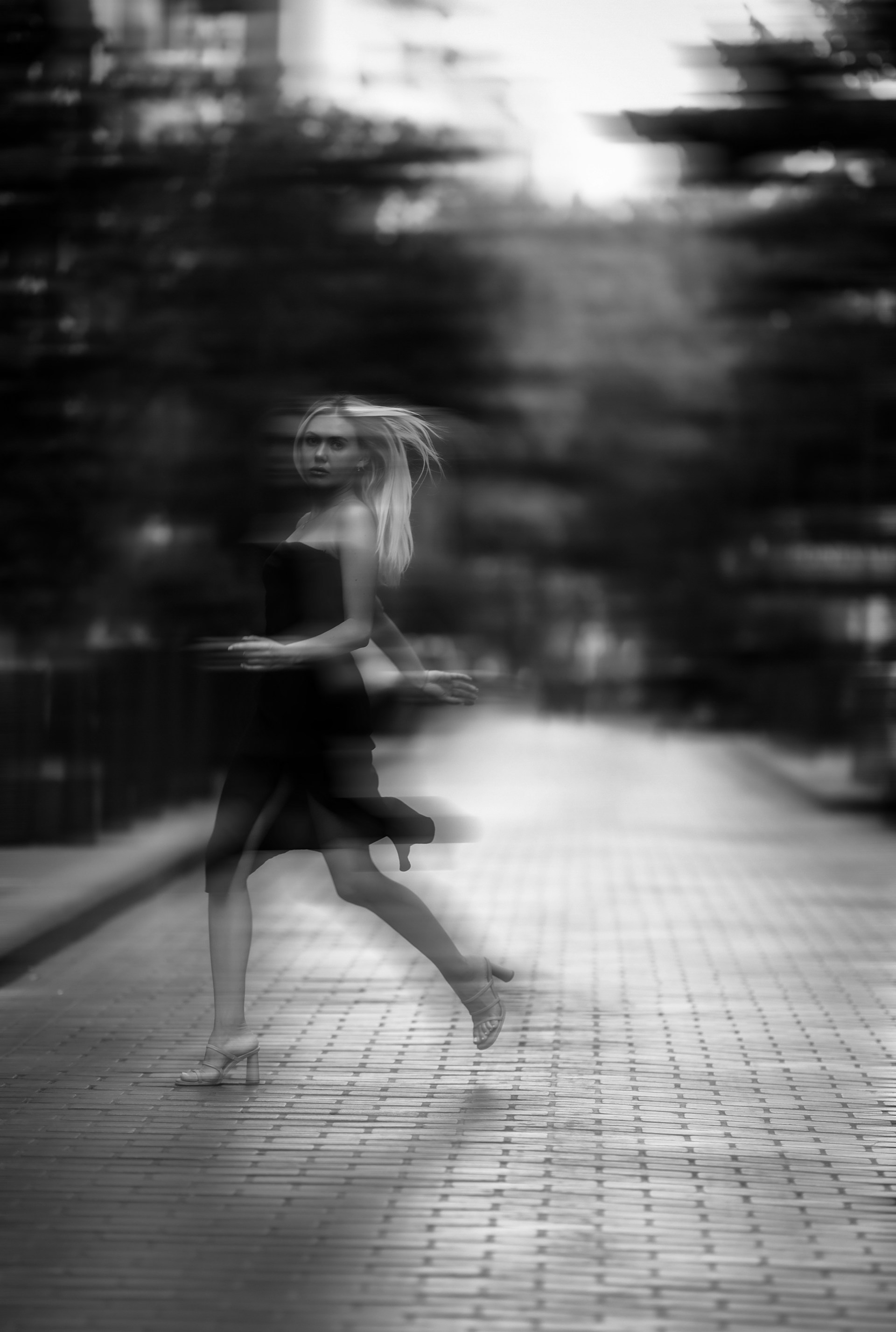 An artistic black and white shot of Yasmin Dream walking down a city street at dusk, hair flowing.