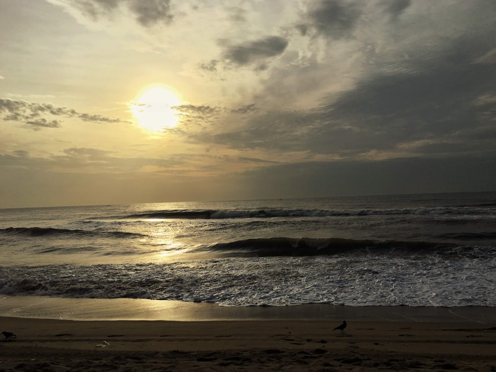 the sun is setting over the ocean on a cloudy day