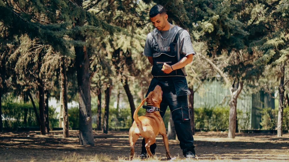 a man standing next to a brown dog in a forest