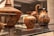 A collection of ancient pottery items displayed in a museum setting, featuring intricate designs and patterns. The pottery includes a large bowl with a lid, a small vase, and a jug, all adorned with animal motifs and floral patterns.
