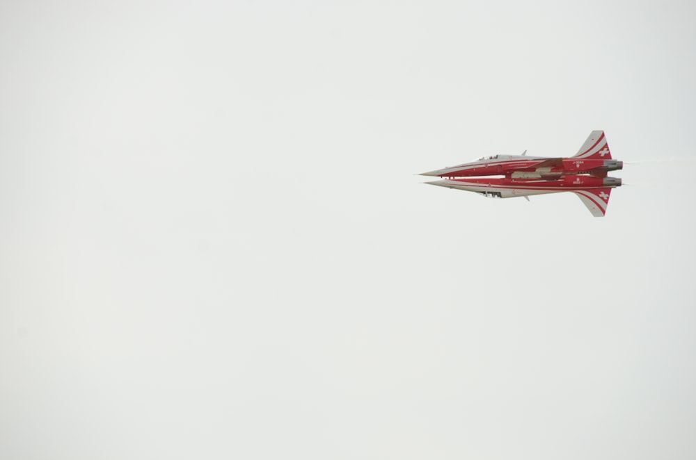 a red and white jet flying in the sky