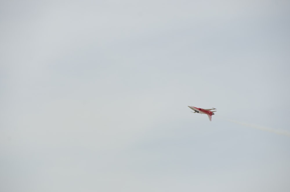 a red and white jet flying through a cloudy sky