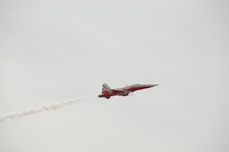 a red and white jet flying through a cloudy sky
