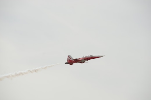 a red and white jet flying through a cloudy sky