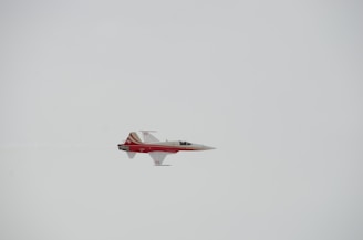 A sleek, red and white jet aircraft is flying through a clear sky. The design includes distinctive markings and streamlined features that suggest speed and agility.
