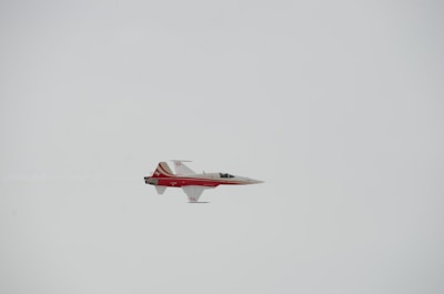 A sleek, red and white jet aircraft is flying through a clear sky. The design includes distinctive markings and streamlined features that suggest speed and agility.