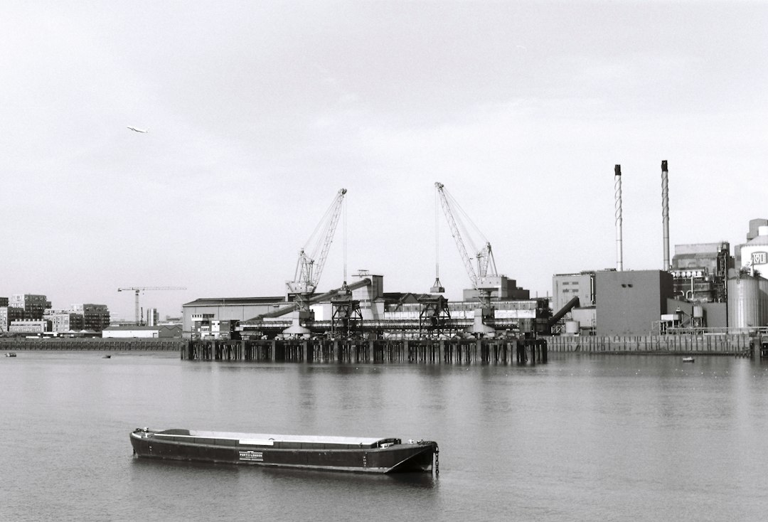 a boat floating on top of a river next to a dock, Ilford FP4 in London.