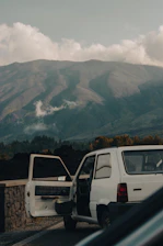 A happy traveler unlocking a rental car door with a scenic American highway in the background.