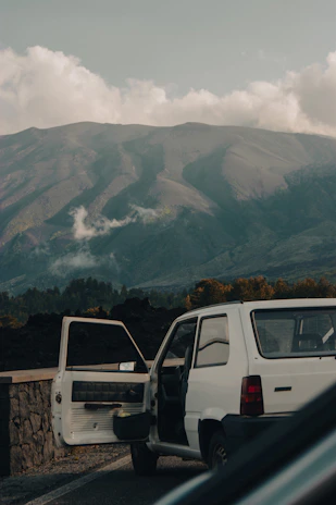 A professional driver opening the door of a comfortable car beside a scenic Lebanese mountain road.