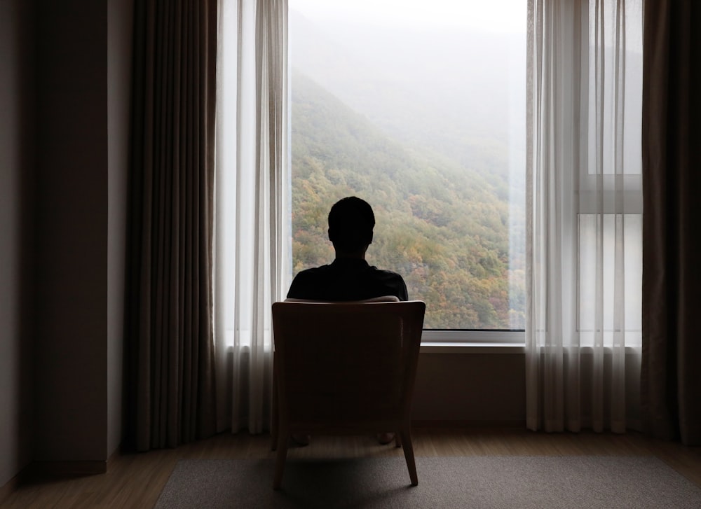 a man sitting in a chair looking out a window