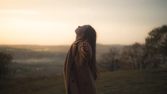 A smiling individual standing on a hilltop at sunset, arms open wide embracing change.