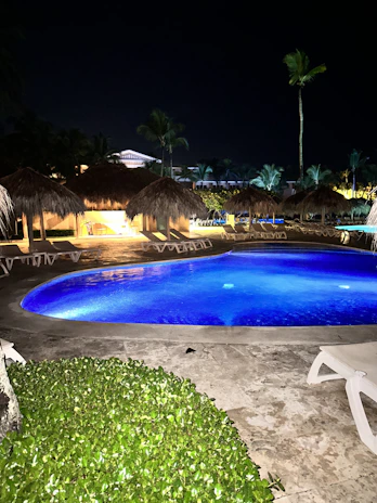 Private pool shimmering under soft lighting, surrounded by lush greenery at dusk.