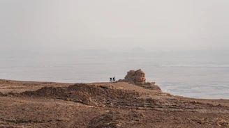 Cyclists navigating a dusty trail winding through red rock desert formations.