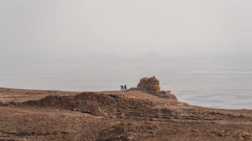 Cyclists navigating a dusty trail winding through red rock desert formations.