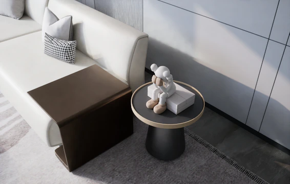 A modern living space features a light-colored sofa with geometric-patterned cushions. A small wooden side table is adjacent to the sofa, and a round side table holds a sitting statue in light tones, possibly resembling a character or figure.