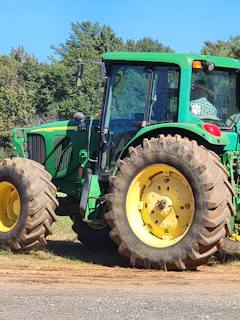 A farmer wearing a hat inspecting a tractor in a sunny farmyard