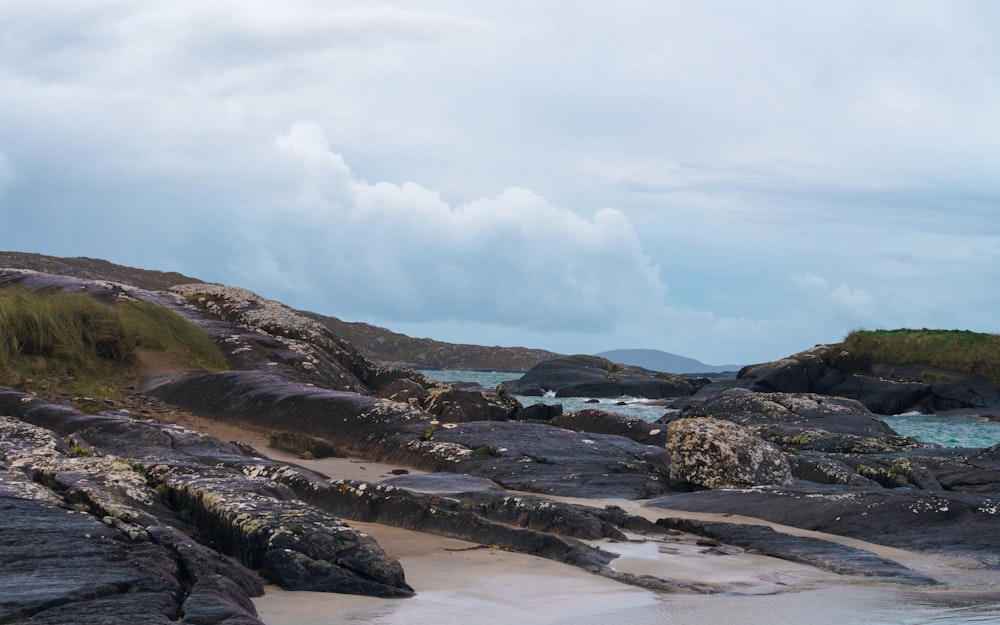 a sandy beach with rocks and water under a cloudy sky