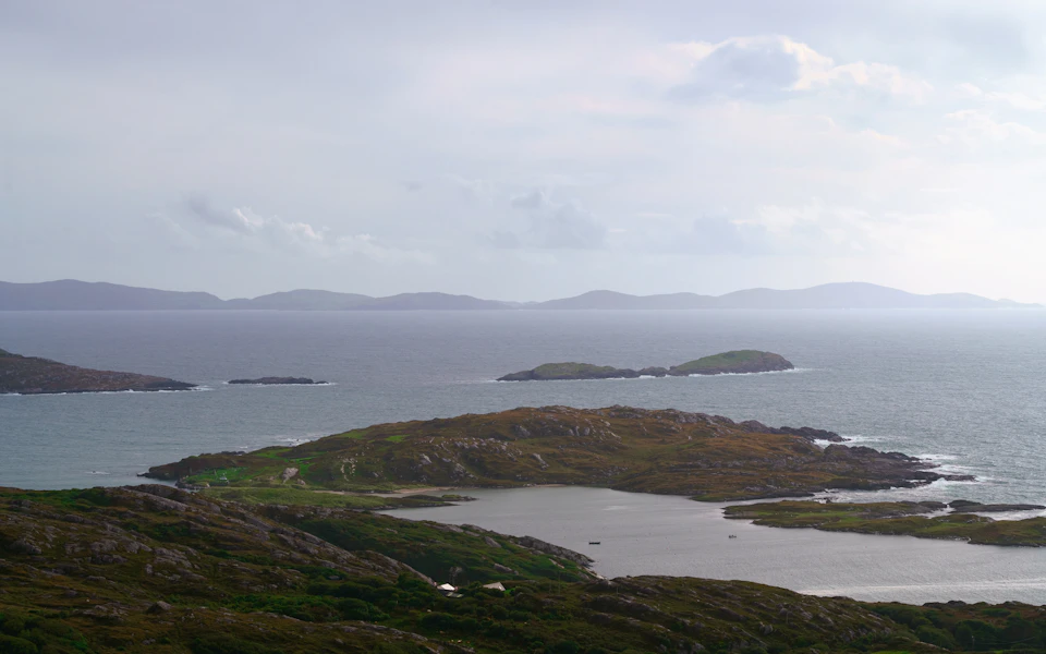 The image depicts a serene coastal landscape with three small islands nestled amidst the vast expanse of the ocean. The islands are scattered across the water, each with its own unique charm and character. The sky above is painted in shades of gray, suggesting an overcast day or perhaps even a storm brewing on the horizon.

The perspective of the image is from a high vantage point, providing a bird's eye view of the scene below. This viewpoint allows for a comprehensive appreciation of the islands' beauty and their relationship to the surrounding ocean. The colors in the image are predominantly gray and green, reflecting the natural hues of the landscape.