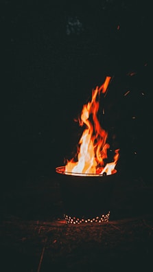 A small fire burning in a metal container, casting warm light on surrounding walls.