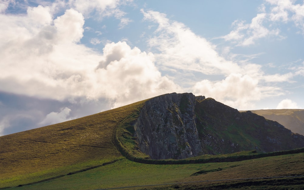 a grassy hill with a large rock face