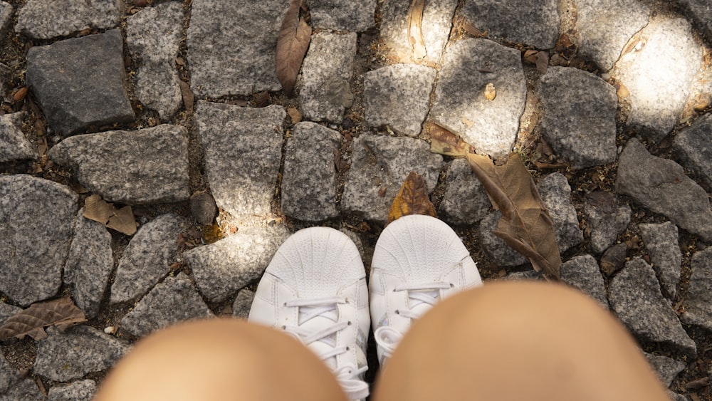 a person wearing white tennis shoes standing on a cobblestone road