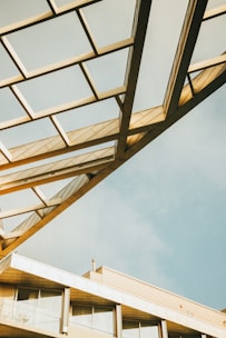 A modern architectural structure with geometric metal framework extending above a building. The design features a series of triangular and rectangular shapes creating a dynamic pattern. The sky in the background is clear with a soft blue hue, adding to the aesthetic appeal.