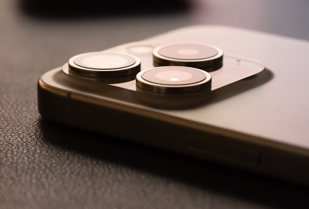 A close-up image of a smartphone's protruding camera lenses, showing three circular lenses on a metallic surface, with a dark, textured background.