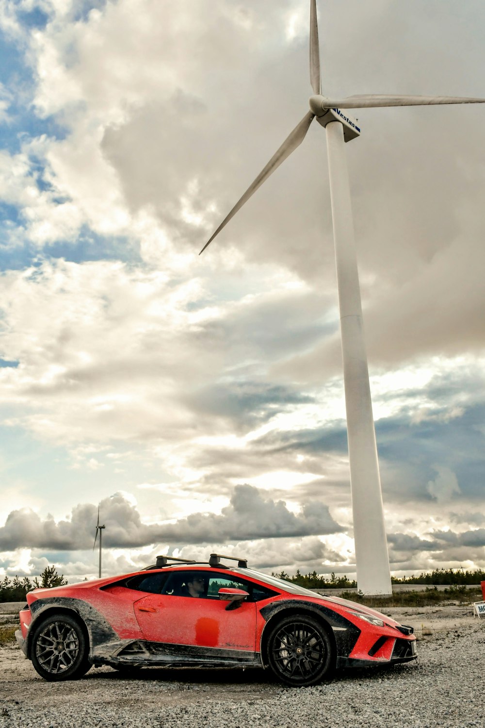 um carro esportivo vermelho estacionado em frente a uma turbina eólica