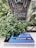 A weathered sign with the word 'BEWARE' and a menacing figure is set among green plants. Below the sign, there is a book titled 'LICANTROPIE' which features a blue cover with a silhouette of a werewolf and a full moon against a starry night sky.
