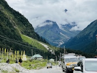 a group of cars driving down a road next to a mountain