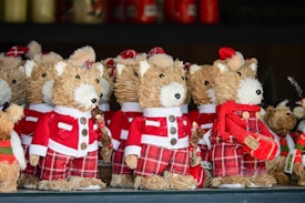 A collection of straw-crafted festive dog ornaments dressed in red and white Santa Claus outfits, with some wearing hats and others adorned with scarves. They feature button eyes and black noses, standing together on a shelf as part of holiday decorations.