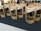 Several brown paper bags with clear windows displaying dried worms are arranged on a dark surface. The bags are labeled with text and graphics, likely indicating the product and brand name. In the background, blurred figures and a bright interior are visible, suggesting a market or exhibition setting.