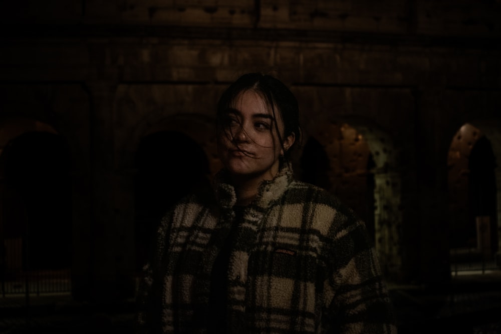 a woman standing in a dark room in a coat