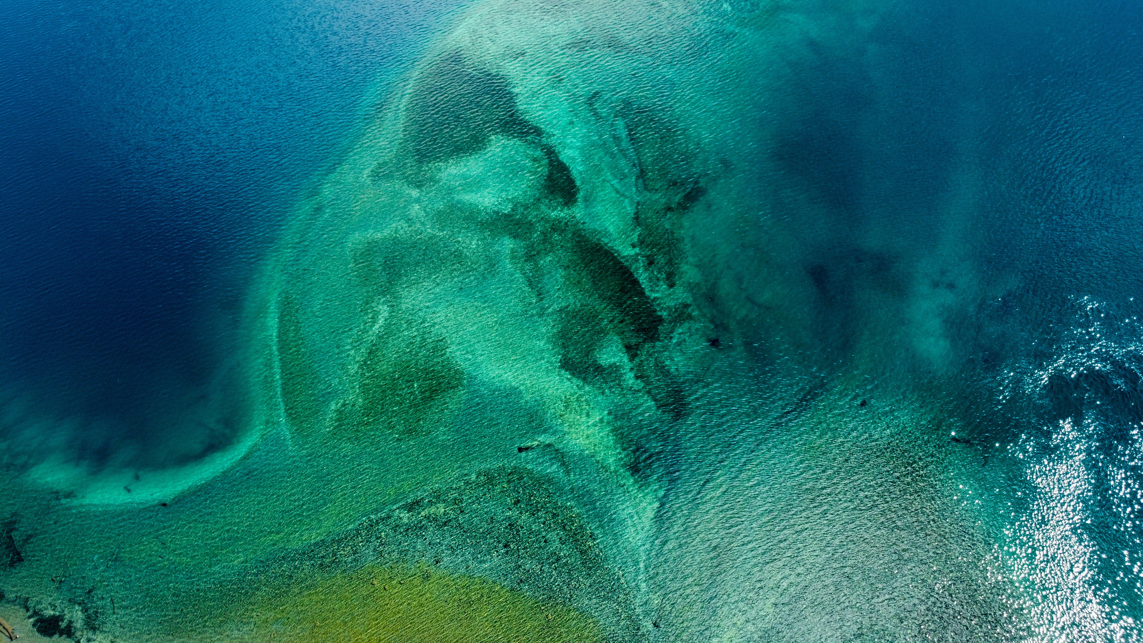 Deep ocean surface with sunlight rays penetrating turquoise water, aerial perspective over vast calm sea
