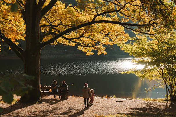 A warm, cinematic photo of a family sharing a quiet moment under terracotta-colored autumn leaves.