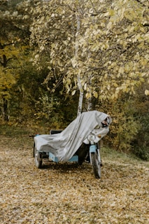 A vintage motorcycle parked beside a rustic garage with autumn leaves around.