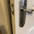 A close-up of a door with a shiny metal handle and latch, slightly ajar. The door is white, and the metal latch is installed on the frame, which appears worn around the latch slot.