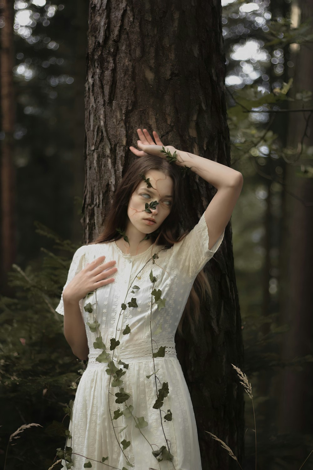 a woman in a white dress standing next to a tree