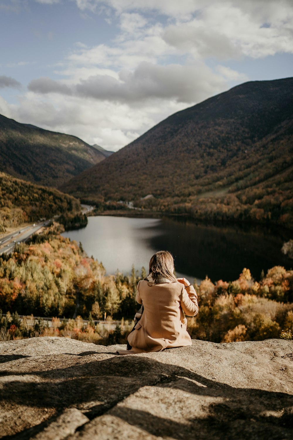 una mujer sentada en lo alto de una roca junto a un lago
