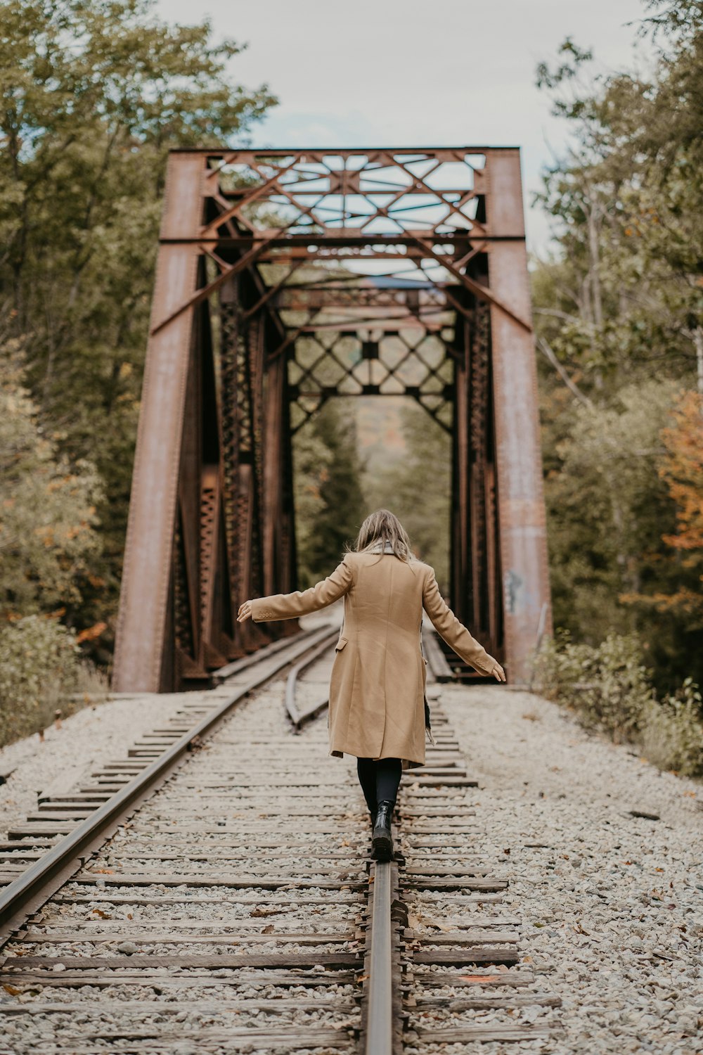 a woman walking across a train track towards a bridge