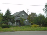 Close-up of a teardown property with an older home surrounded by mature trees.