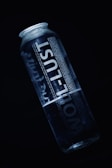 A clear plastic bottle labeled 'WOL-LUST' is prominently displayed against a dark background. The bottle is partially filled with water and the text on the bottle is printed in a bold, white font. The overall lighting is dark, emphasizing the transparency and simplicity of the bottle.